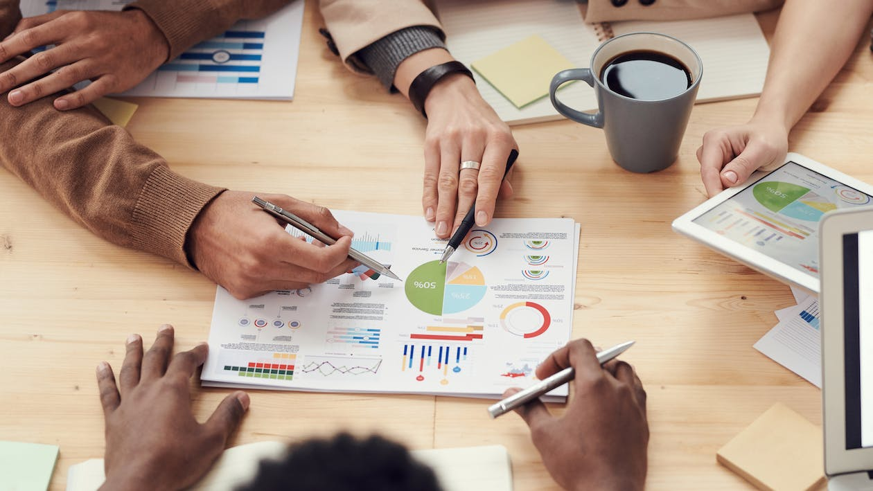 Several people focus on a sheet of paper that has several line graphs and pie charts made on it.